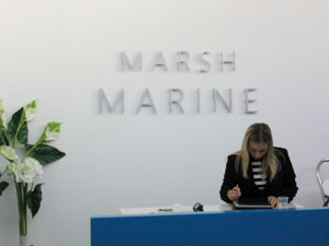 A woman sat at a blue desk with the words 'Marsh Marine' on the wall behind her