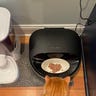 Overhead shot of an automatic pet food feeder with wet food in it and and orange cat