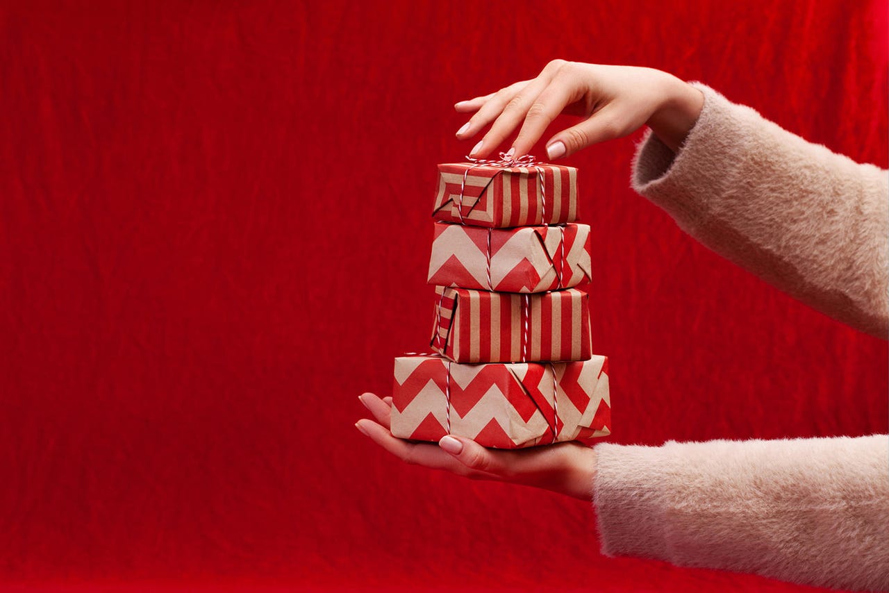 Hands holding a stack of wrapped presents against a red background.