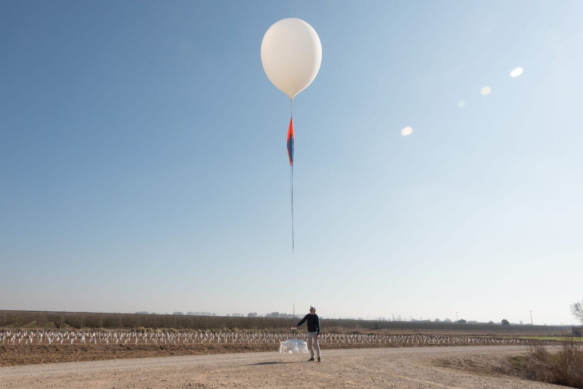 A person in a flat field with a large white balloon overhead