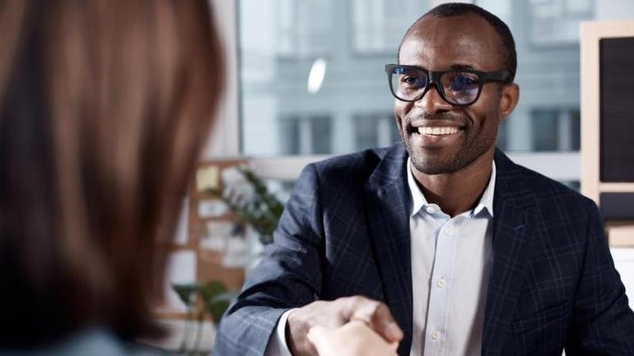 Black man wearing glasses smiling and shaking a white woman's hand