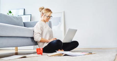 Female student sitting on floor of her apartment with laptop and notes studying