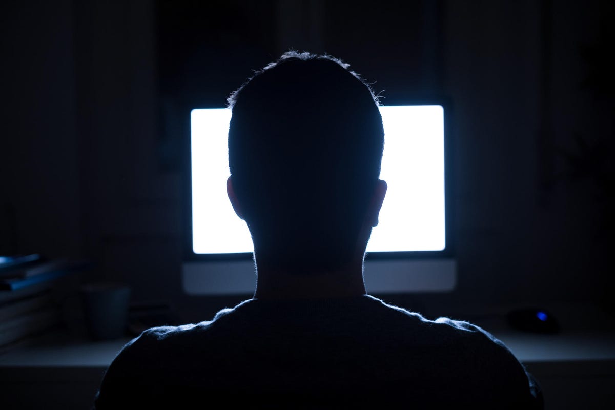 Silhouette of a person's head in front of a lighted computer screen at night.