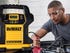 A DeWalt portable jump starter resting on an open engine compartment of a car while a man connects the battery clamps.