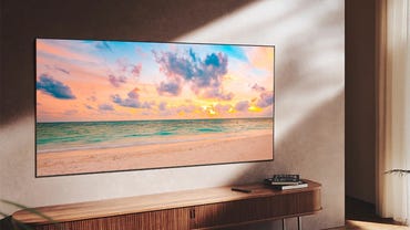 Samsung QN90B television wall mounted above a console table. The screen is showing a beach scene at sunset.