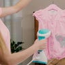 Image of a woman using a steamer on pink baby clothing.