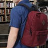 Man wearing a red backpack with shelves of books in the background
