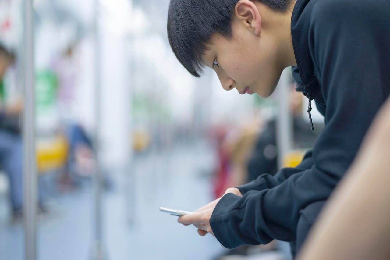 Asian teenage boy using smart phone on the MRT