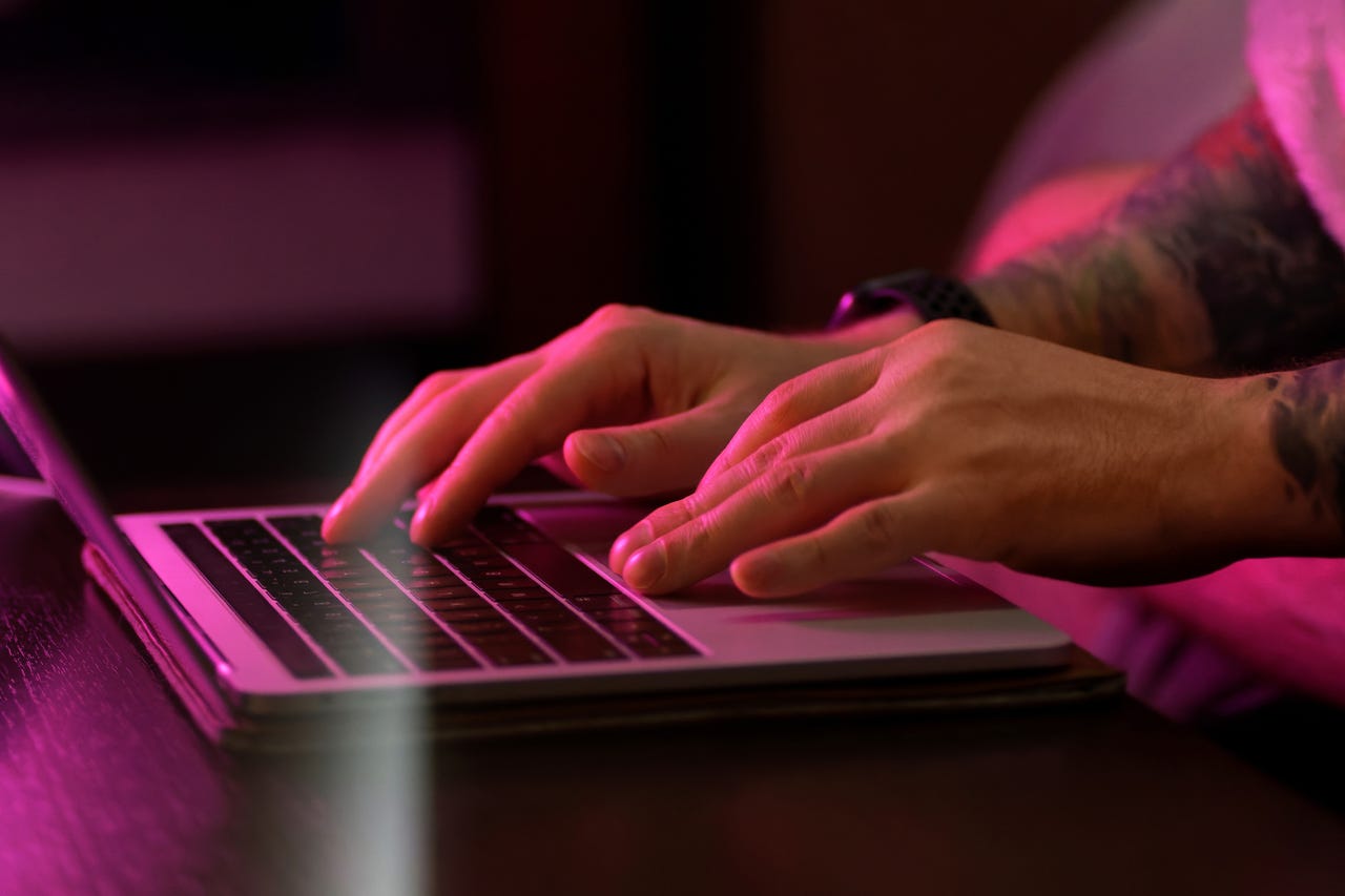Close up of male hand typing on laptop keyboard in neon light