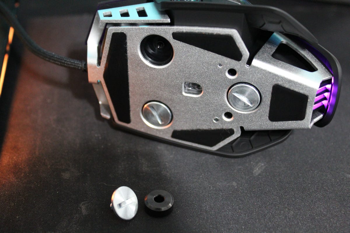An underside view of the Corsair M65RGB Ultra mouse with one of its weights removed and sitting next to the mouse.