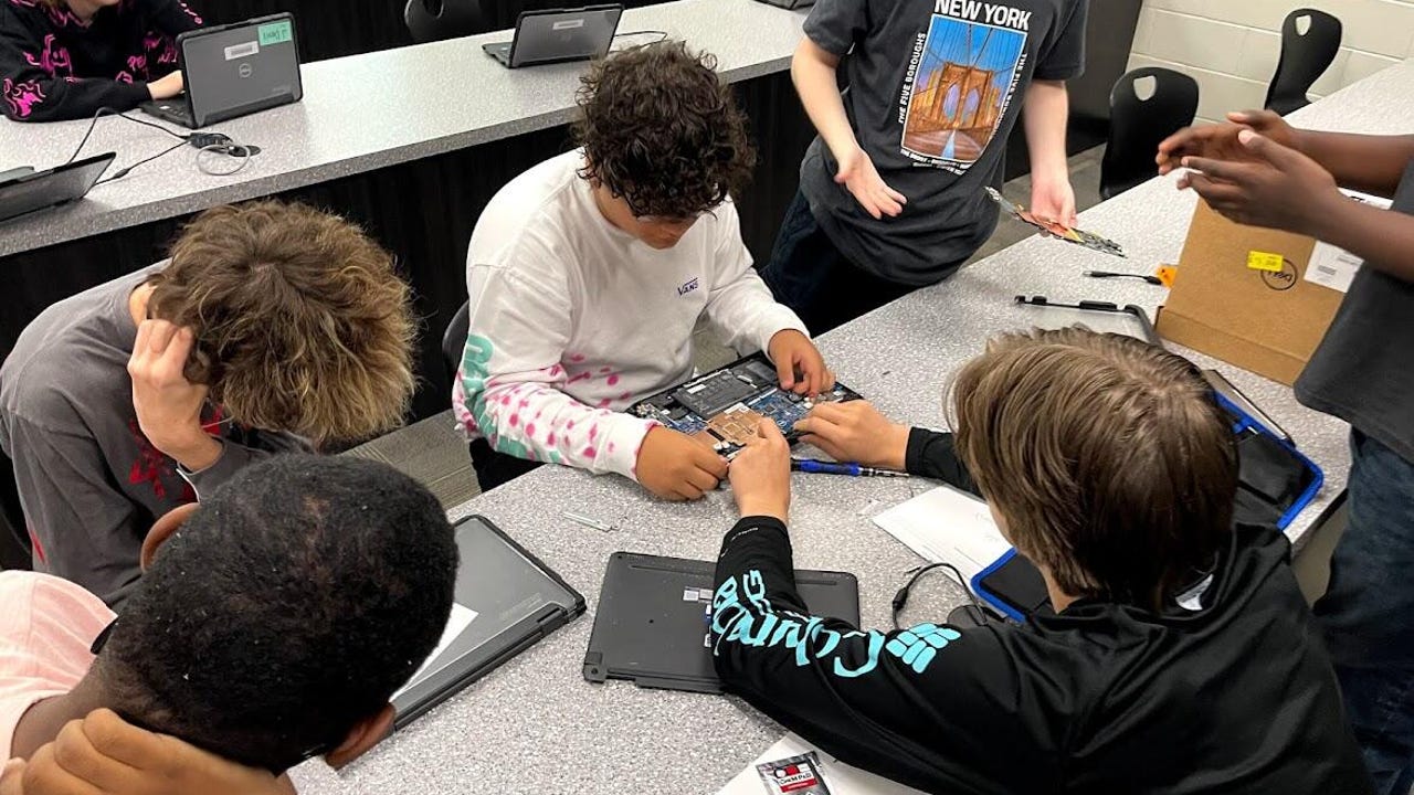 North Augusta High School students sit at long tables troubleshooting broken laptops.