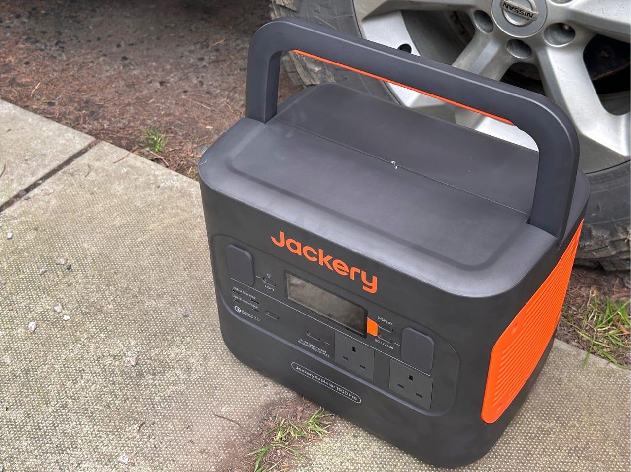 The Jackery Explorer 1500 Pro portable with the handle lifted, outdoors next to a car
