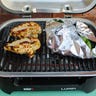 Close-up of two chicken breasts and a foil packet of broccoli being cooked on a Weber Lumin electric grill