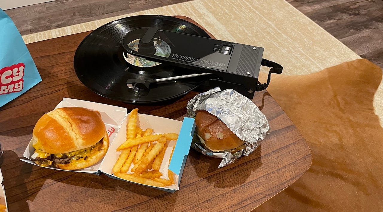 A vinyl record player with burgers and fries on the table