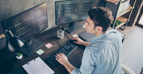 white man with brown hair sitting in front of two computer monitors