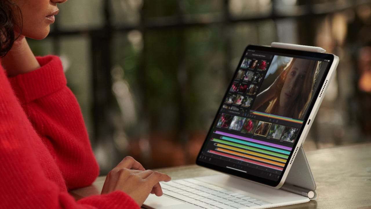 A woman in a red sweater uses an iPad Pro with keyboard attachment to edit a video.