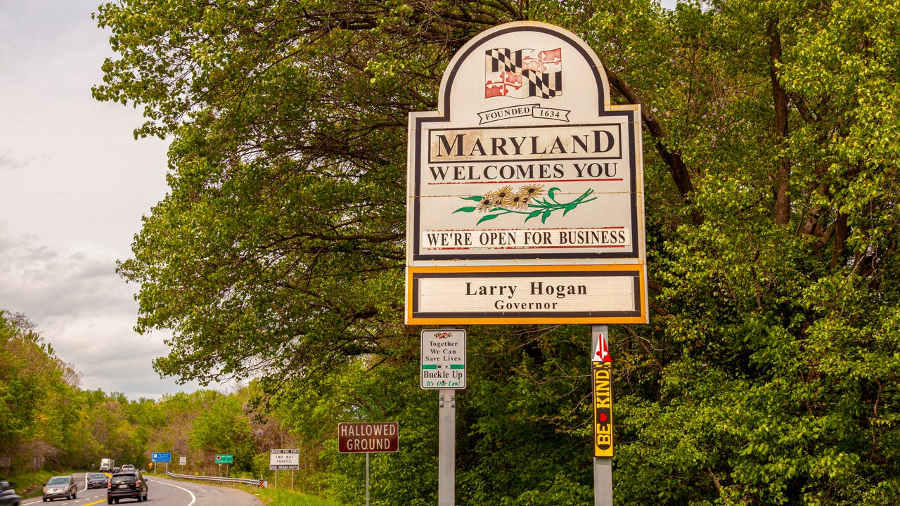 A sign welcoming people to Maryland beside a tree-lined road.