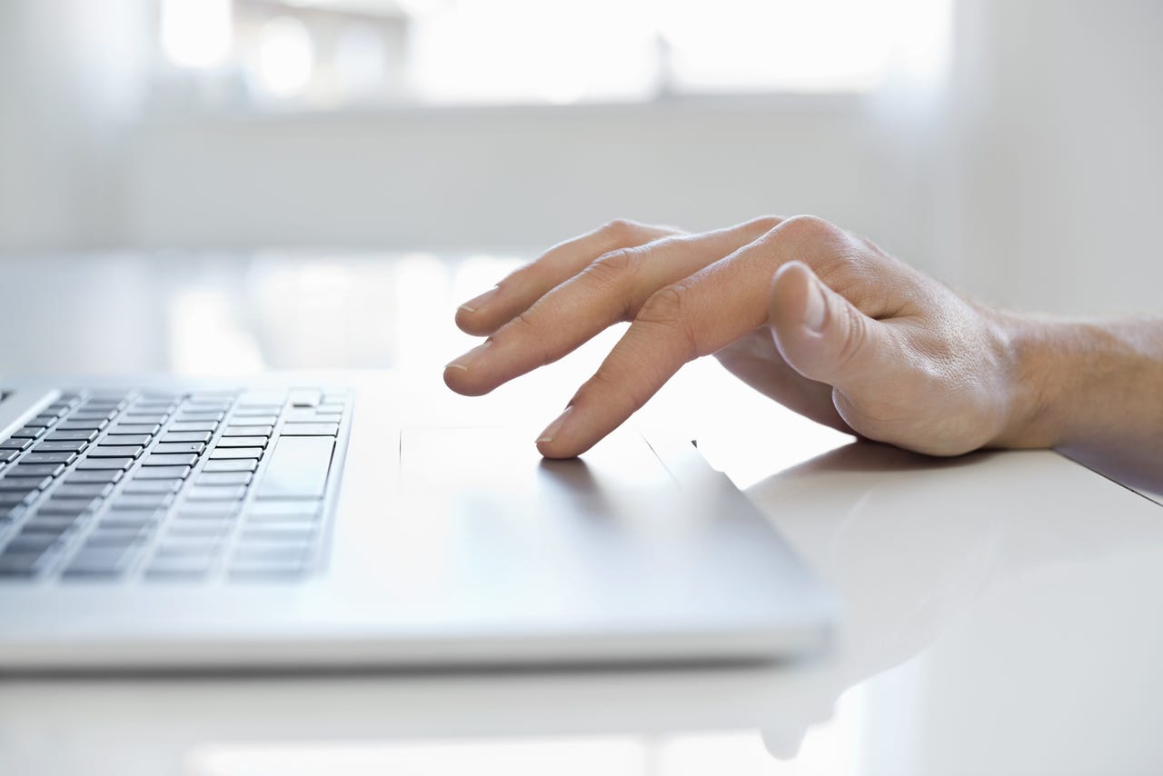 La mano de un hombre adulto medio usando el panel táctil en una computadora portátil en casa