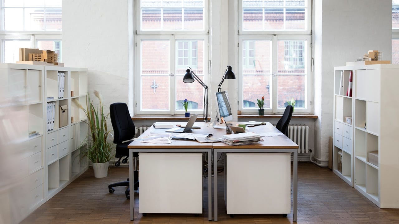 A bright empty office with two desks sitting by a window facing each other
