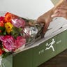 Woman unboxing a bouquet of multi-colored roses from a green FTD box