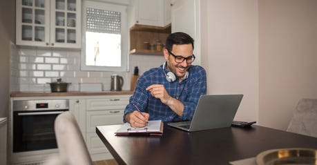 man working at computer and writing things down on notebook