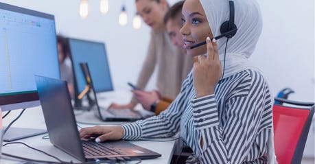 woman in hijab speaking to someone on a headset in front of a computer