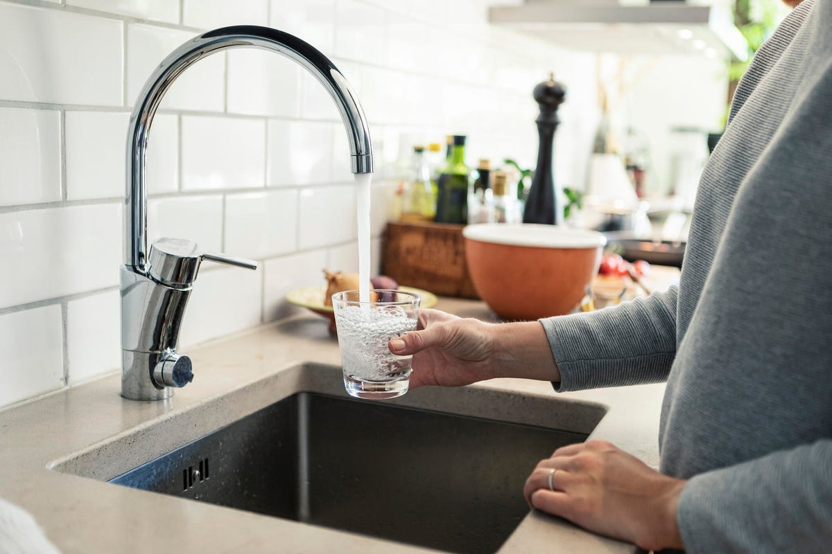 a-woman-holding-a-glass-of-water-under-a-kitchen-tap