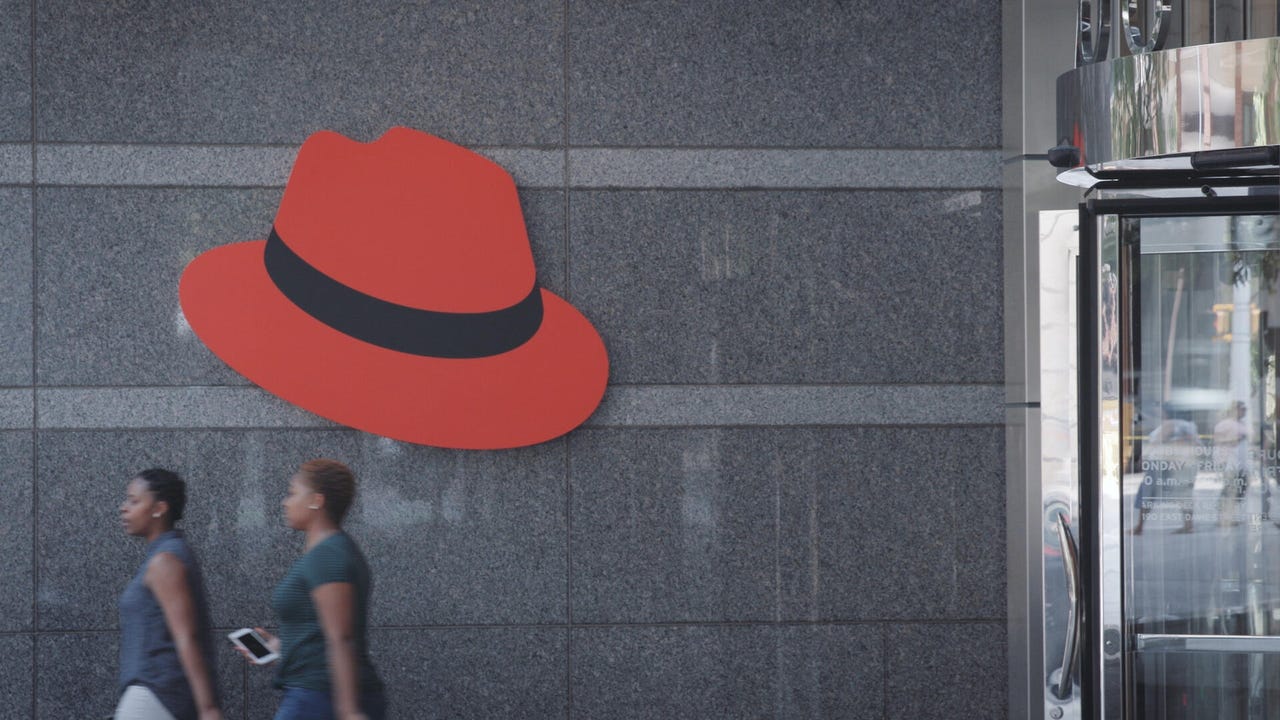 People walking by red hat on the wall.
