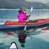 Woman in an inflatable kayak on a lake with mountains in background