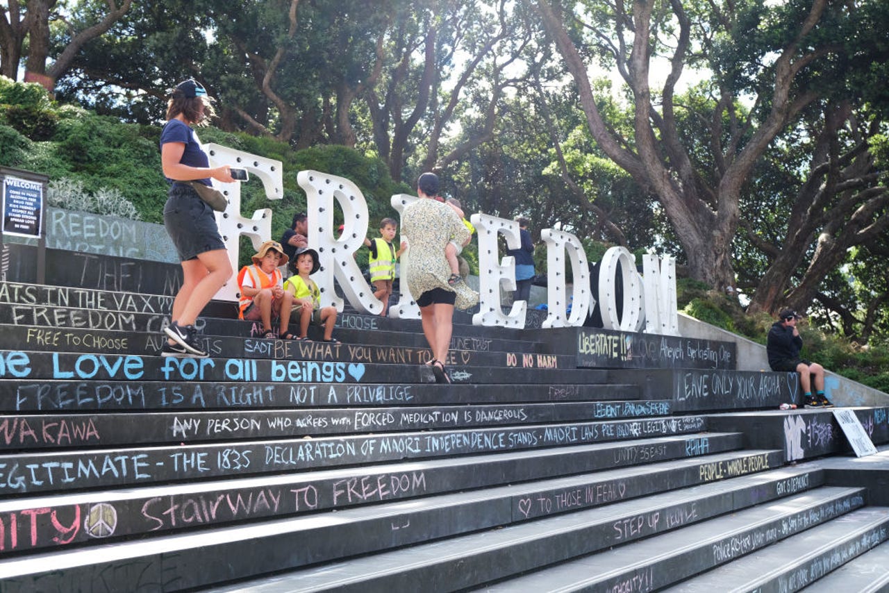 A family with young children sits near the large 'Freedom' lightbox sign erected by protestors on the steps leading to the Beehive on February 18, 2022 in Wellington, New Zealand.