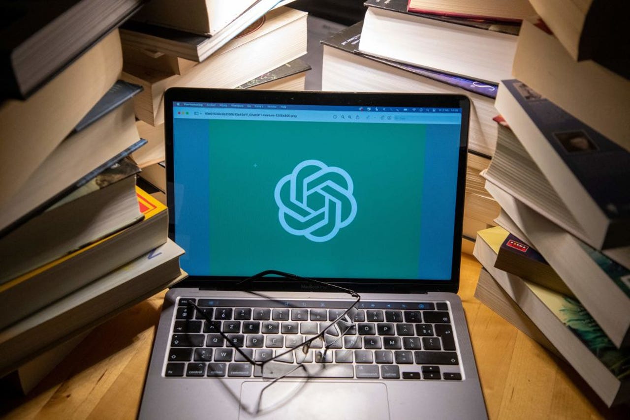 OpenAI logo on laptop surrounded by books