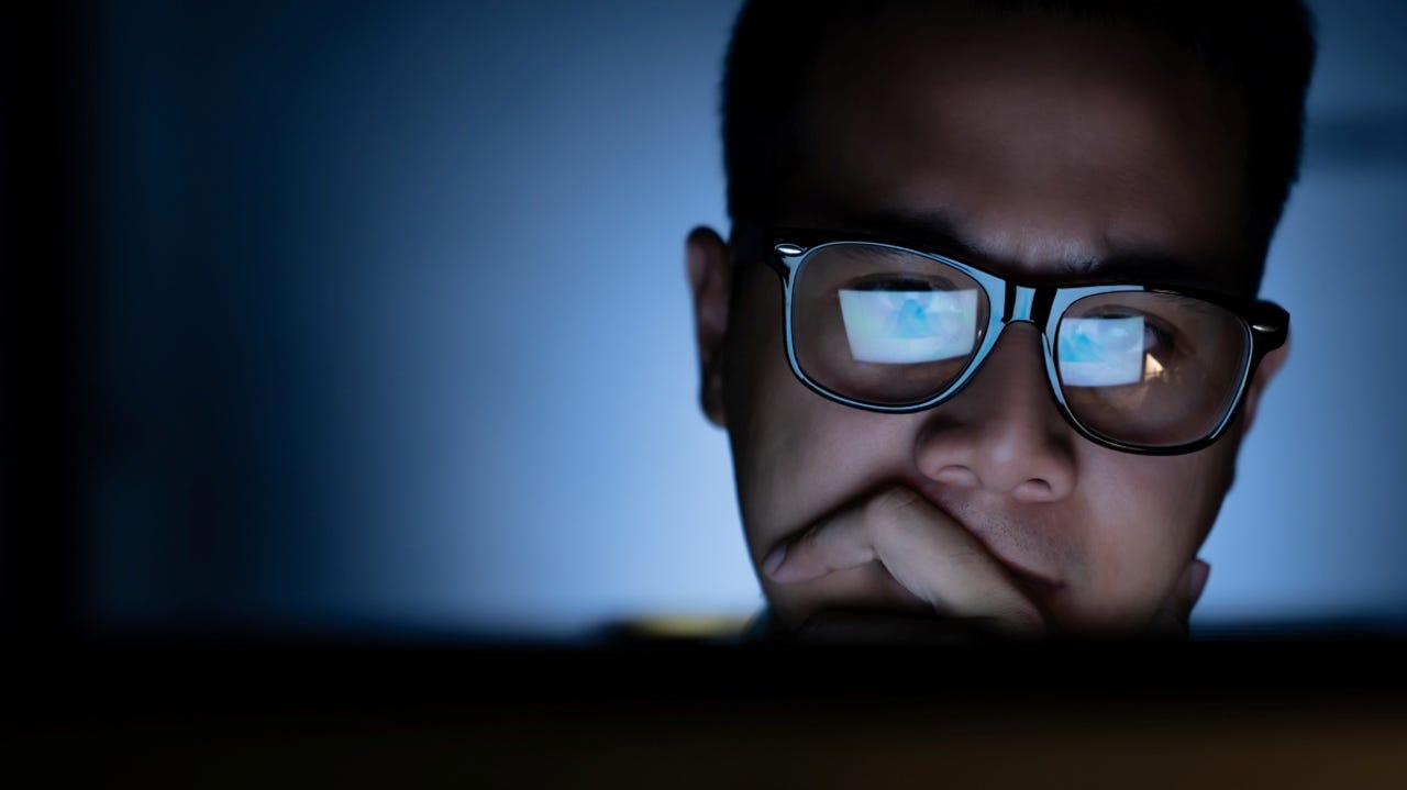 Man with glasses focusing on computer screen with intense expression