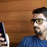 A younger, bearded man wearing Gunnar Intercept blue light blocking glasses while using his smartphone.