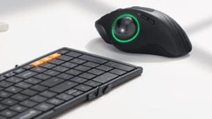 Mouse preto com um trackball grande ao lado de um teclado preto
