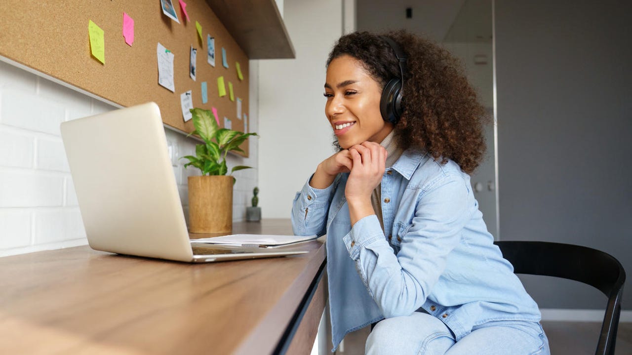 Smiling Black woman wear headphones video calling on laptop.