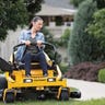 A woman in work clothes using a Cub Cadet Ultima ZT1 to mow around a concrete walkway