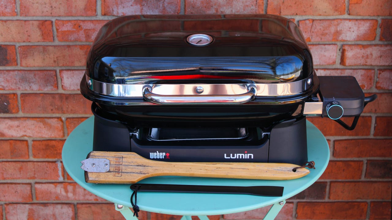 Close-up of the Weber Lumin electric grill on a table with a grill brush and spatula.