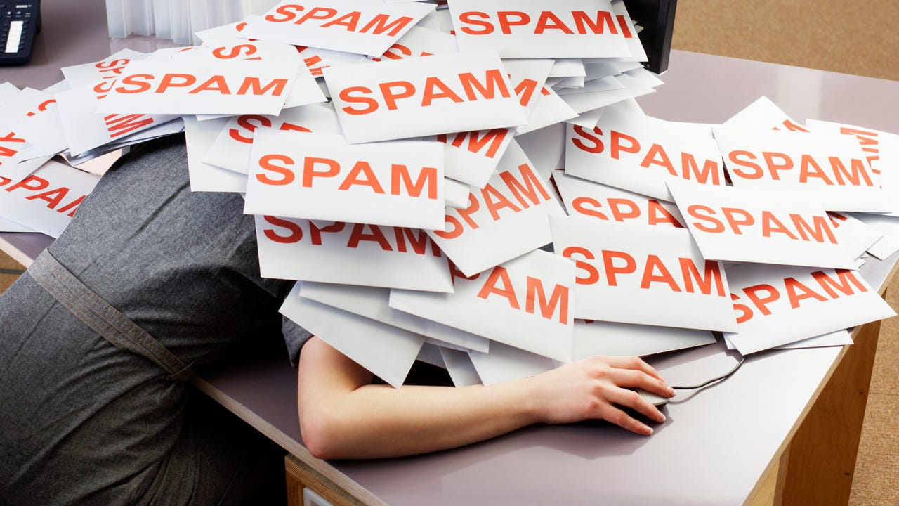 Person collapsed on desk under pile of papers that say spam