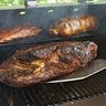 Close-up of someone removing a smoked brisket, rack of ribs, and pork roast from a Pit Boss 700FB pellet grill.
