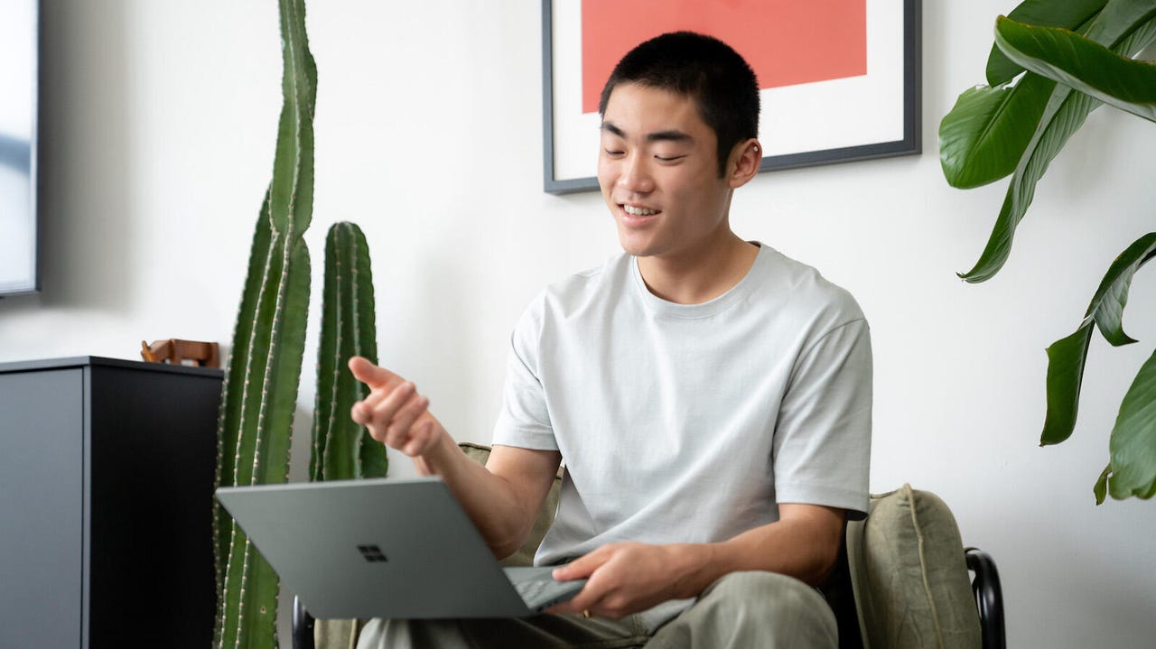 A seated man is using a Microsoft Surface Laptop