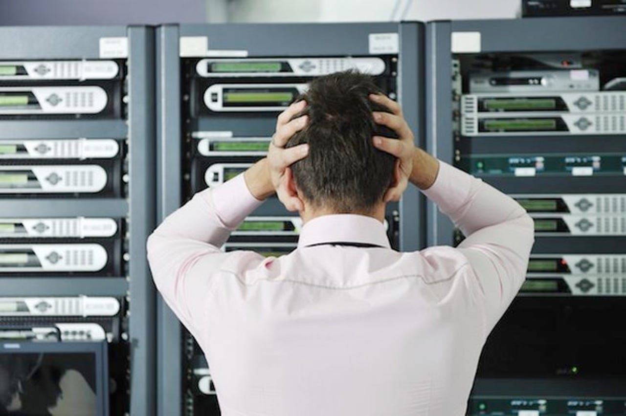 Person holding their head in distress looking at a server rack