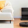 A Roborock vacuum on the floor next to a couch and its black base