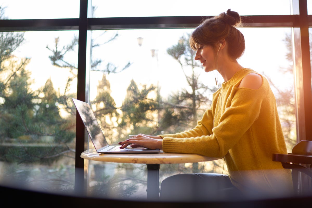 زنی پشت میز کافه آفتابی از لپ تاپ استفاده می کند.