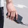 Image of a person holding a Anker 313 Power Bank with a smartphone while crossing a street.