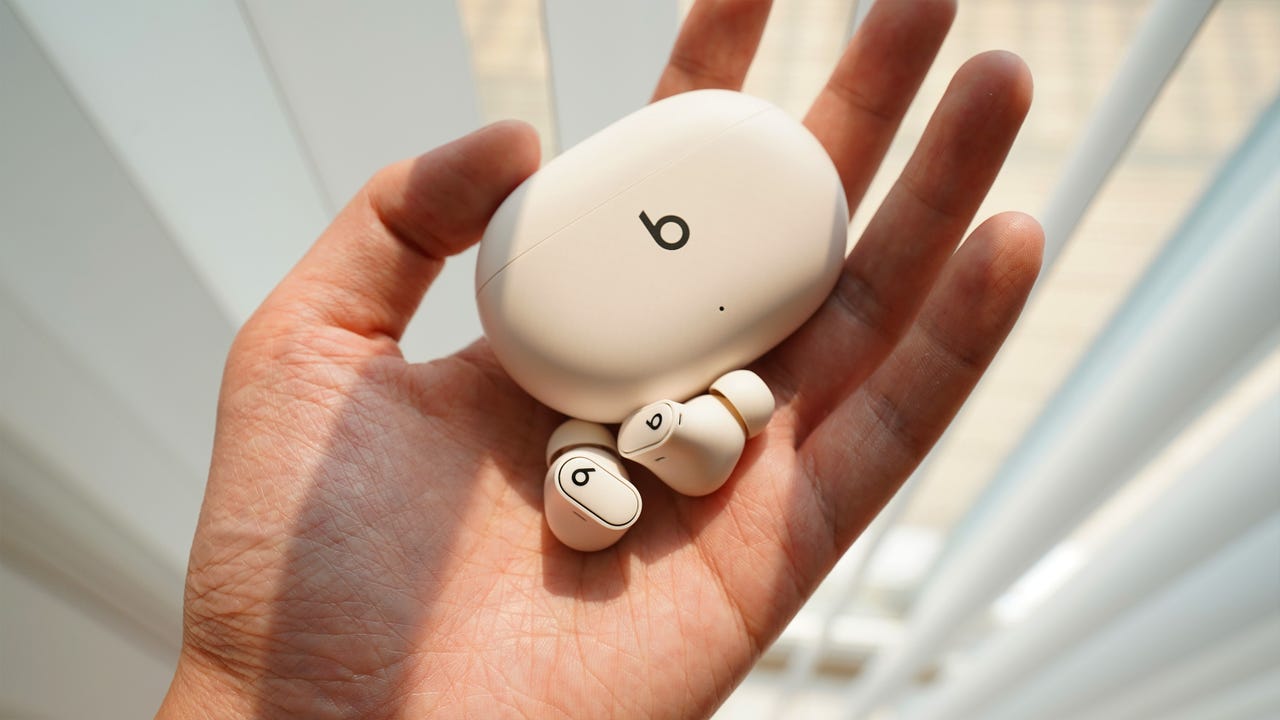 A hand holding up the Beats Studio Buds Plus in Ivory