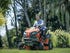 Man riding a Husqvarna lawn mower, cutting grass around a group of palm trees and ornamental flowers