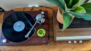 An overhead shot of a vinyl record playing on a record player next to a receiver with a plant on top of it