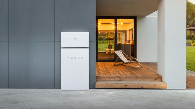 A Tesla Powerwall+ mounted on the dark exterior wall of an ultra-modern home