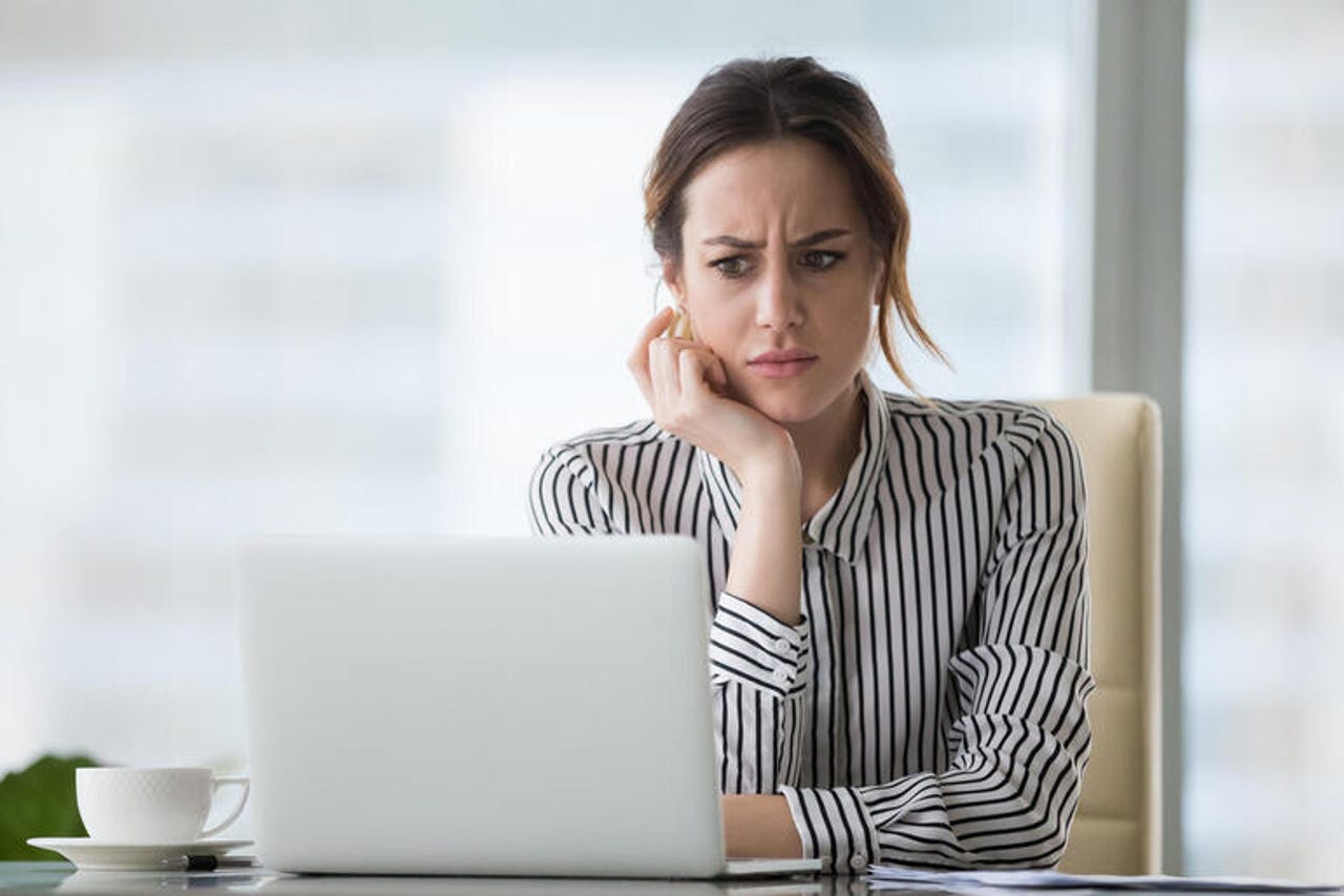 Businesswoman in office looking at laptop, annoyed and confused