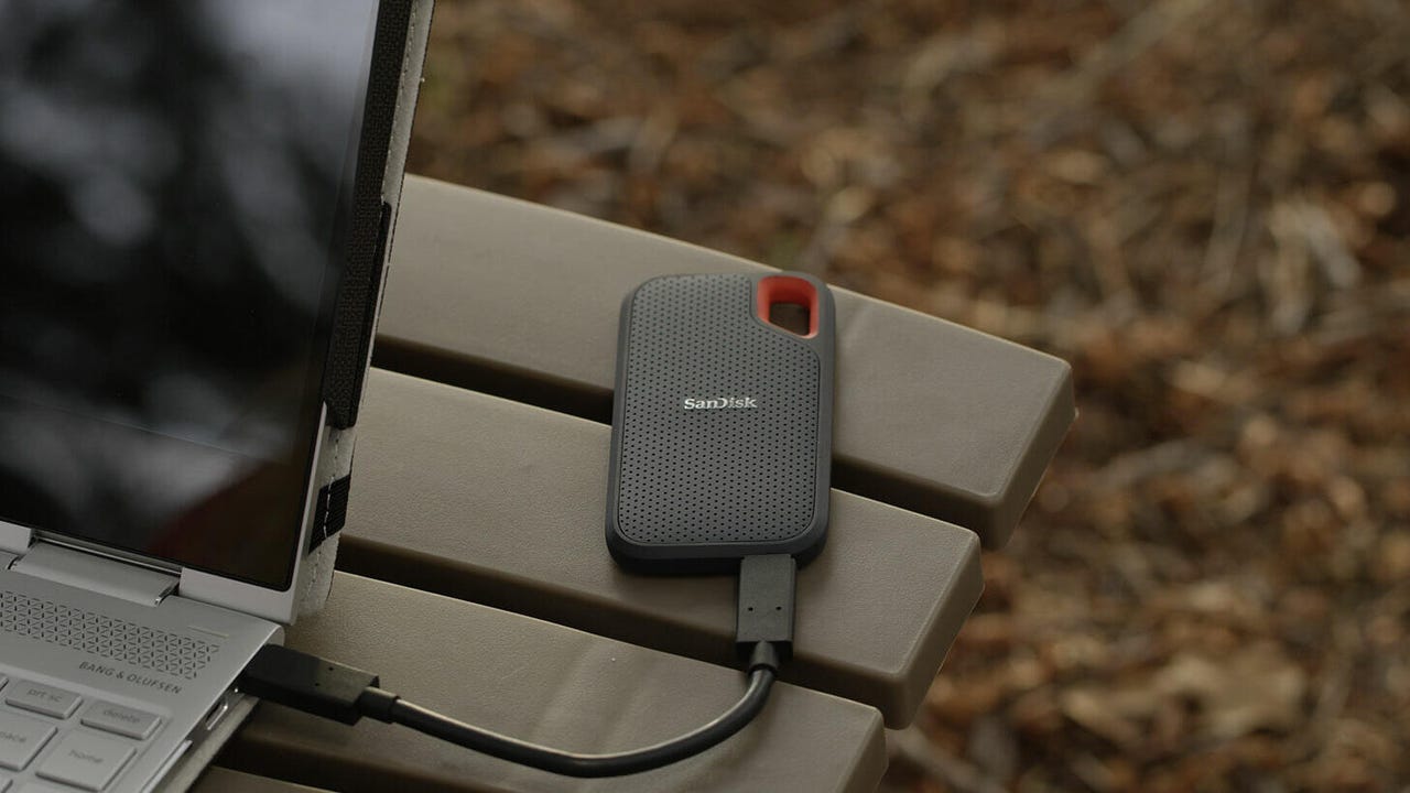 A SanDisk Extreme portable SSD connected to a laptop. Both are resting on a picnic table
